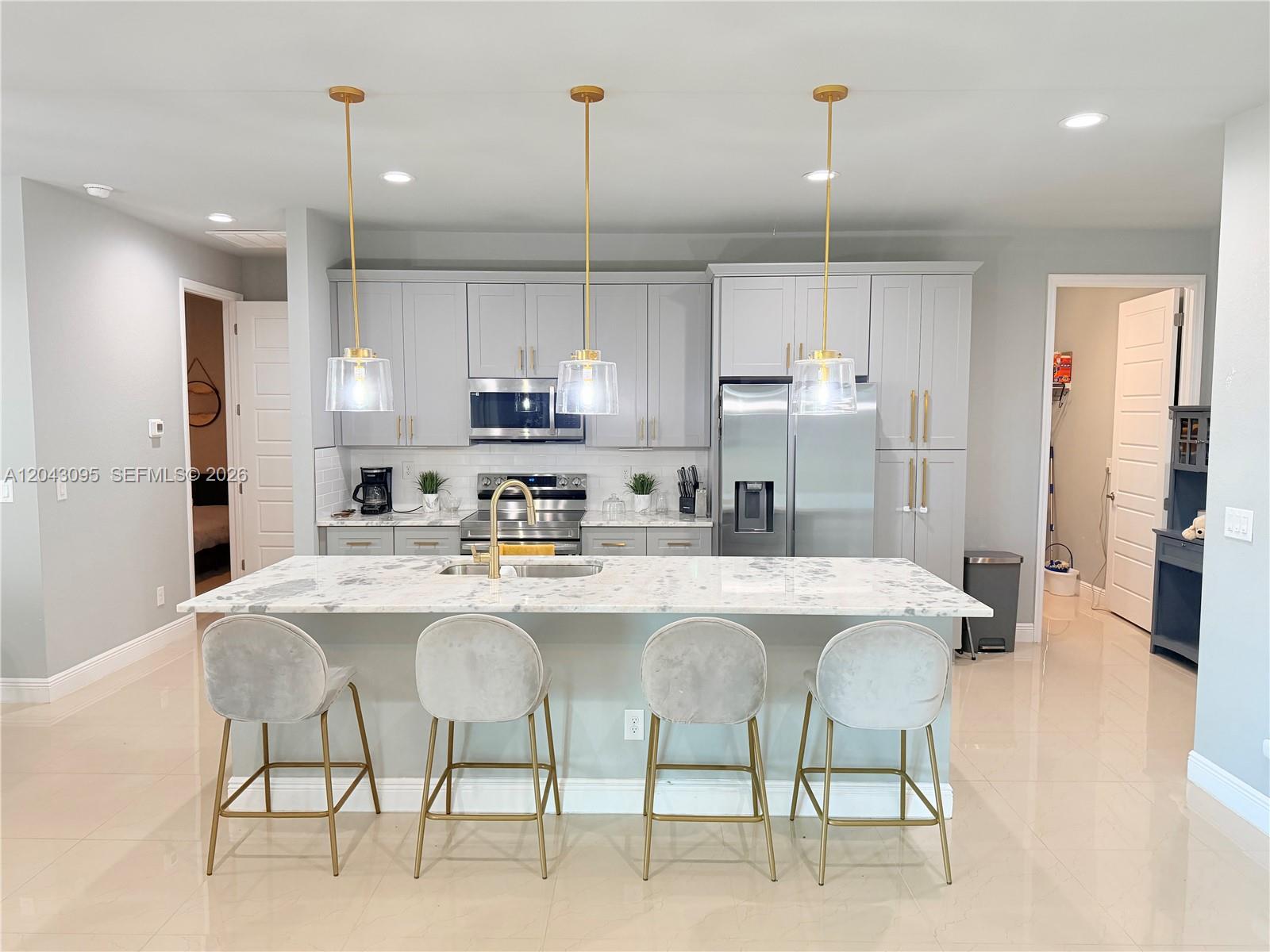 A modern kitchen features gray cabinetry, a marble-topped island with four stools, and gold lighting — 106 Plantation Dr, La Belle FL 33935, LA BELLE, FL