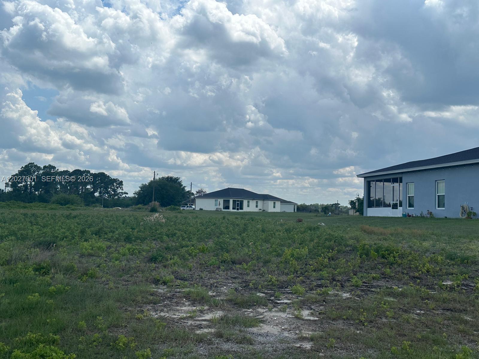A view of a grassy lot with two houses under a cloudy sky — 9020 MAC Ct, La Belle FL 33935, LA BELLE, FL