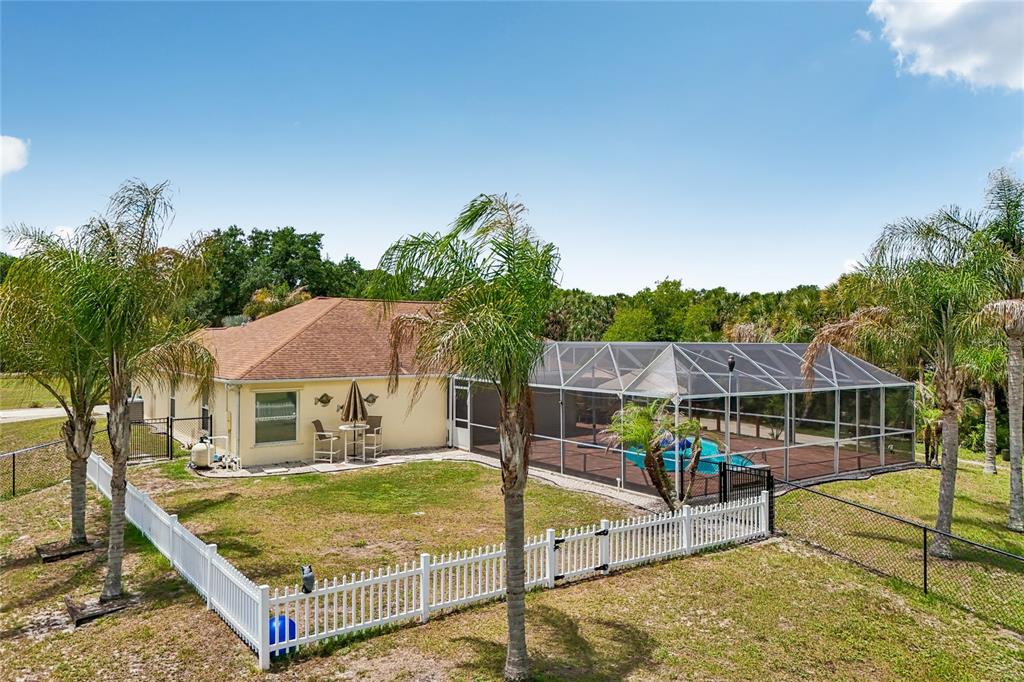 A backyard features a house with a screened-in pool, a white fence, and palm trees — 4880 DATE PALM, COCOA, FL