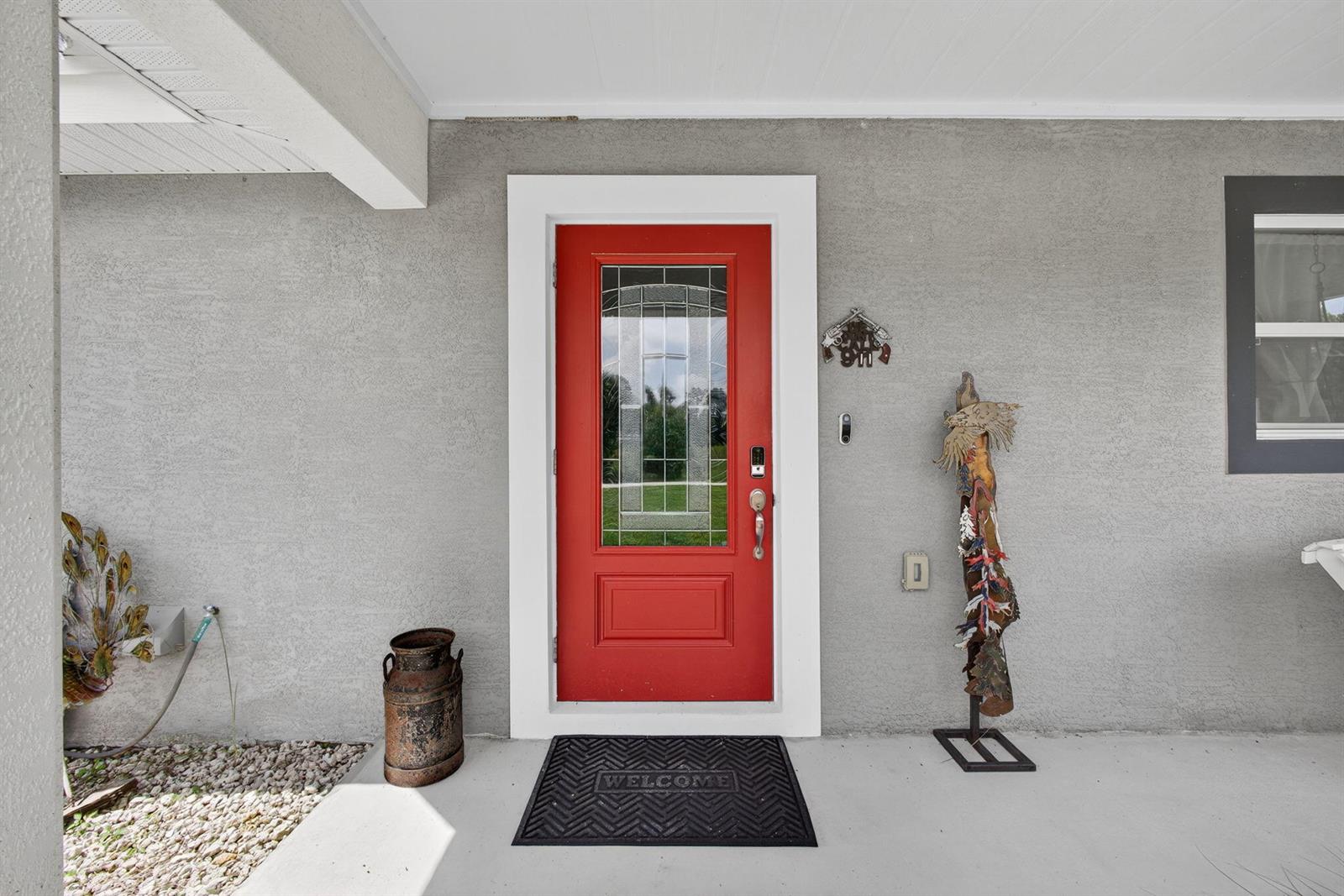 A red front door with a glass insert is centered on a gray stucco wall — 14171 Biddex Road, FL 33470, FL