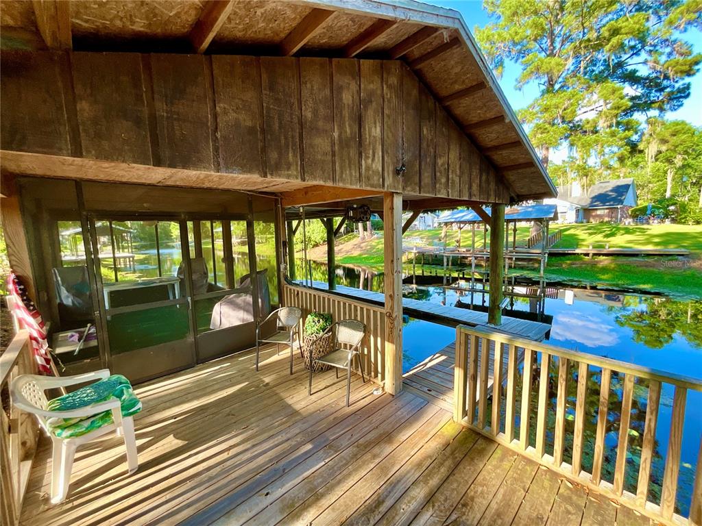 A wooden deck with a screened-in area overlooks a canal with boat docks and trees — 529 SE 5TH AVENUE, MELROSE, FL