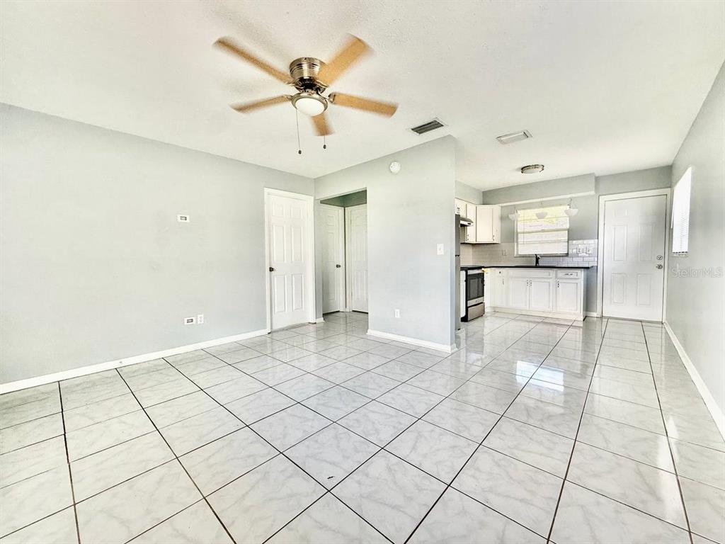 A room with white tile floors, a ceiling fan, and an adjacent kitchen area — 10812 HANNAWAY DRIVE UNIT C, RIVERVIEW, FL