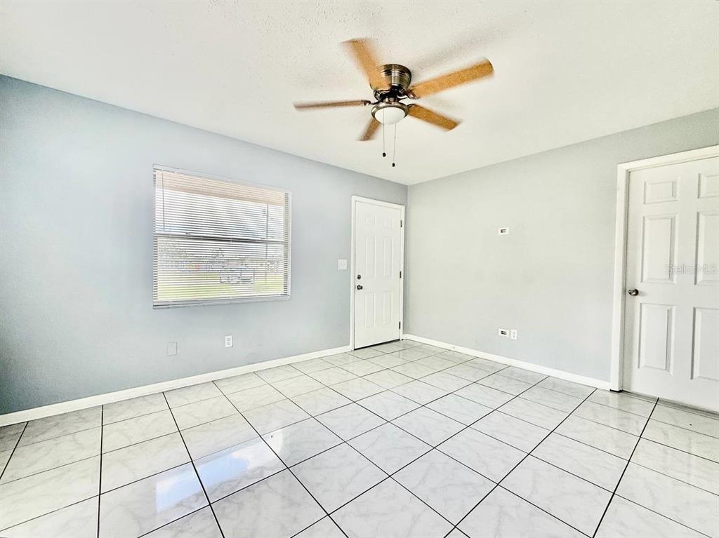 An empty room features light blue walls, white tile flooring, a ceiling fan, and two doors — 10812 HANNAWAY DRIVE UNIT C, RIVERVIEW, FL