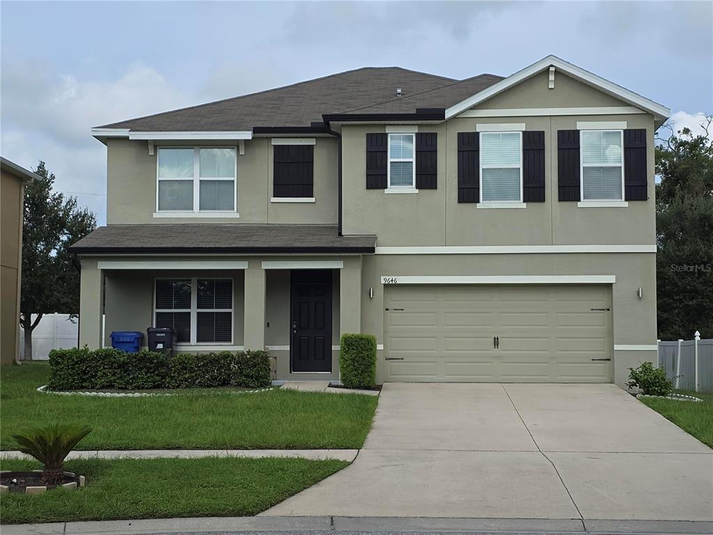 A two-story suburban house with a tan stucco exterior, a two-car garage, and a front porch — 9646 TRONCAIS, THONOTOSASSA, FL