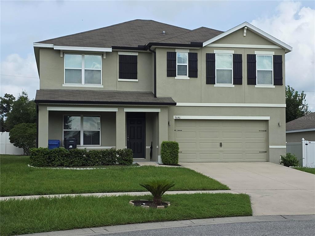 A two-story suburban house with a tan stucco exterior, a two-car garage, and dark shutters — 9646 TRONCAIS, THONOTOSASSA, FL