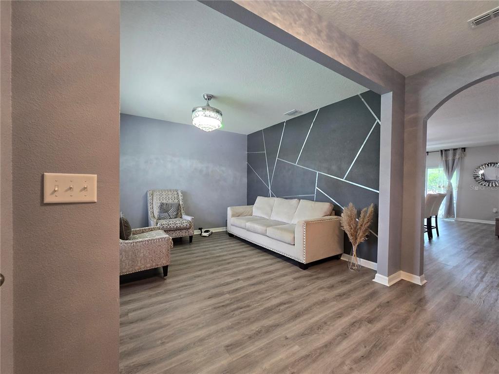 A living room features a geometric accent wall, light-colored sofa, two patterned chairs, and flooring — 9646 TRONCAIS, THONOTOSASSA, FL