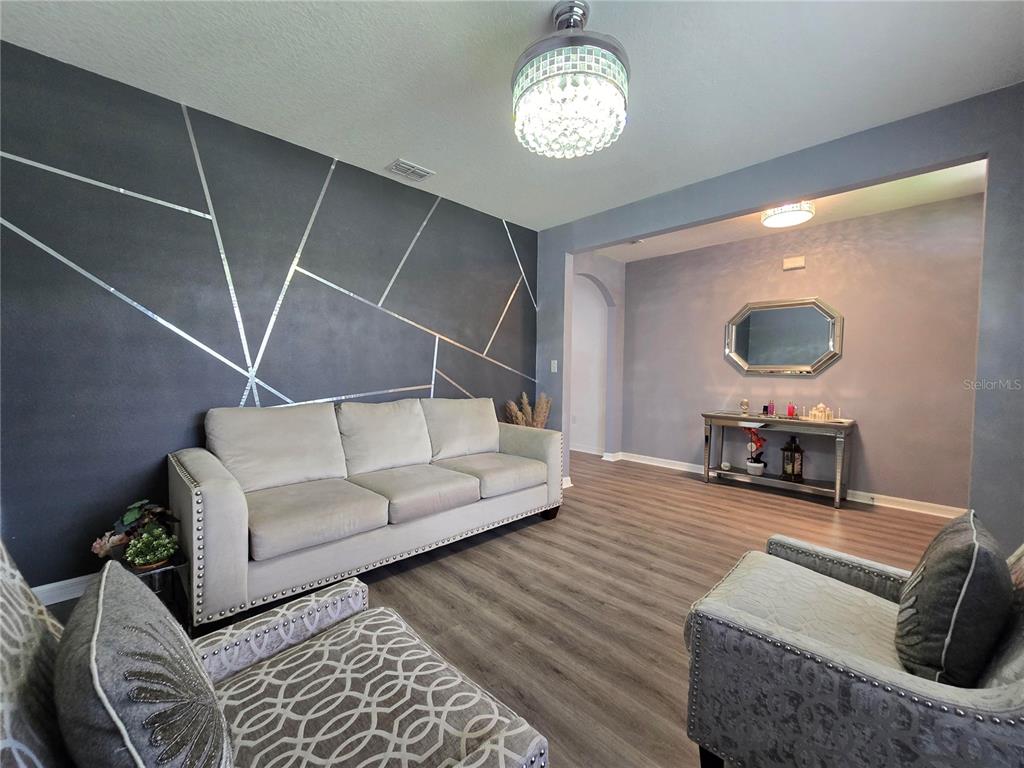 A living room features a geometric accent wall, a light-colored sofa, and wood-look flooring — 9646 TRONCAIS, THONOTOSASSA, FL