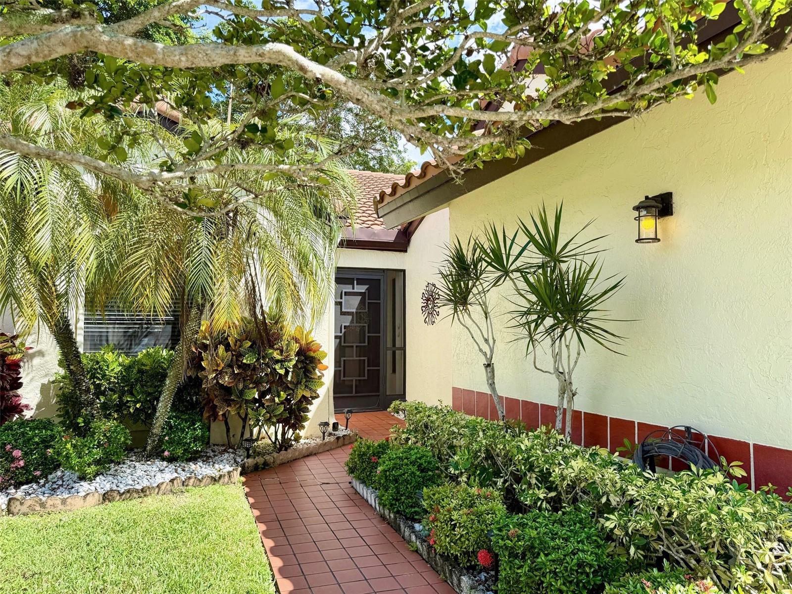 A tiled walkway leads to the front entrance of a house with light-colored stucco walls — 5462 Palm Springs Lane # A, Boynton Beach FL 33437, BOYNTON BEACH, FL