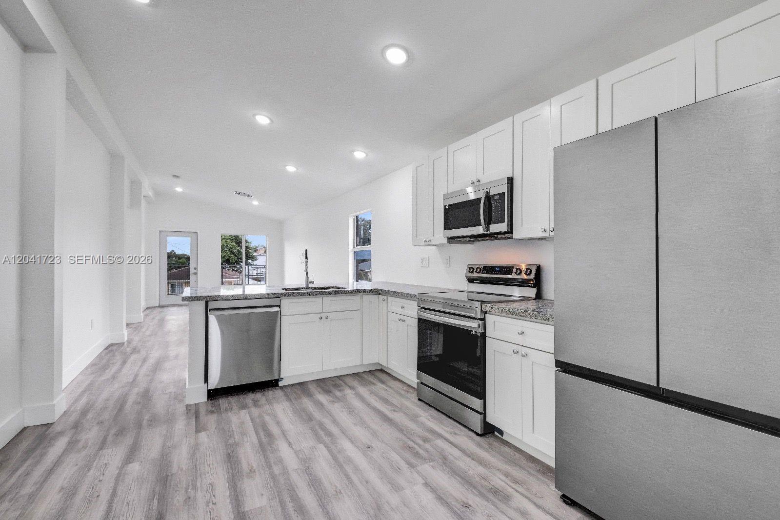 A modern kitchen features white cabinets, stainless steel appliances, and gray wood-look flooring — 7777 NW 8th Ct # A, Miami FL 33150, MIAMI, FL