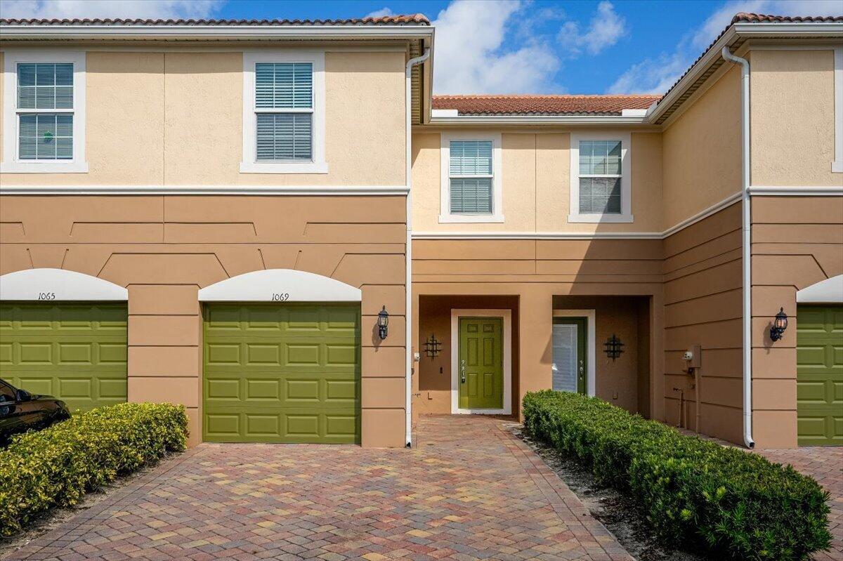 A two-story townhouse exterior features tan stucco walls, green garage doors, and a brick driveway — 1069 Normandie Way, Vero Beach FL 32960, VERO BEACH, FL
