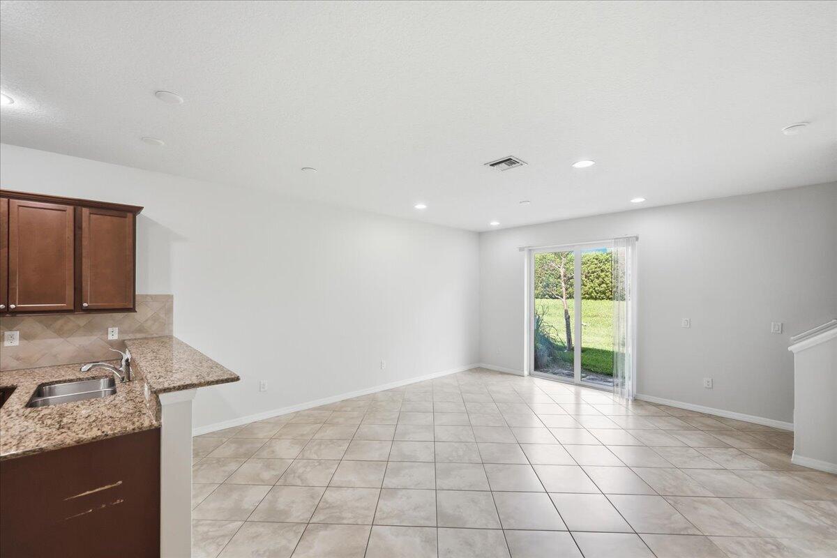An open-concept kitchen and dining area features tile flooring, granite countertops, and sliding glass doors — 1069 Normandie Way, Vero Beach FL 32960, VERO BEACH, FL