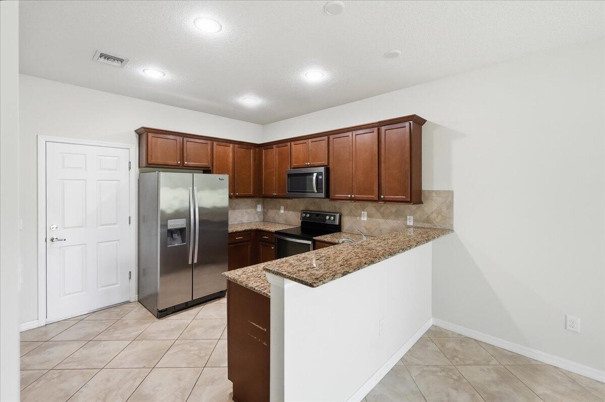 A kitchen features wood cabinets, granite countertops, stainless steel appliances, and tile flooring — 1069 Normandie Way, Vero Beach FL 32960, VERO BEACH, FL