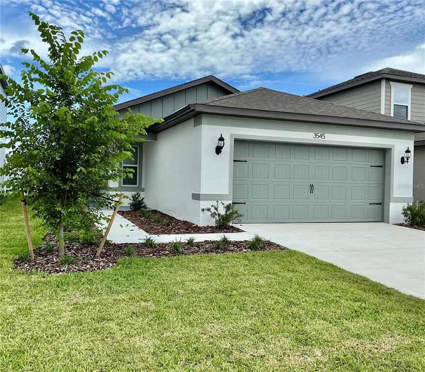 A single-story house exterior features a gray garage door, white stucco walls, and landscaping — 3545 HORNBEAM ROAD, SPRING HILL, FL