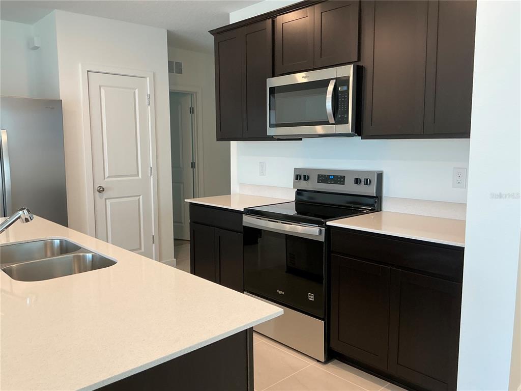 A kitchen features dark wood cabinets, stainless steel appliances, and a white quartz island countertop — 3545 HORNBEAM ROAD, SPRING HILL, FL
