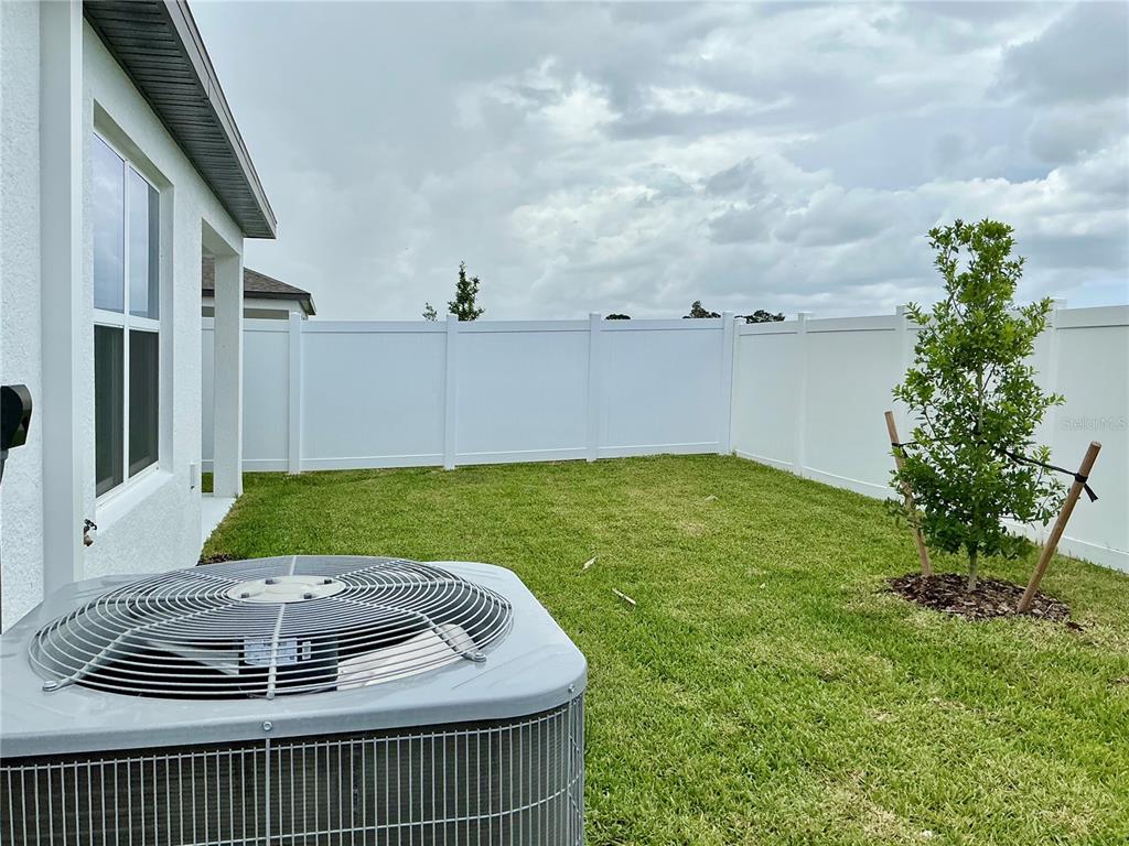 A backyard features a white vinyl fence, a small tree, and an air conditioning unit — 3545 HORNBEAM ROAD, SPRING HILL, FL
