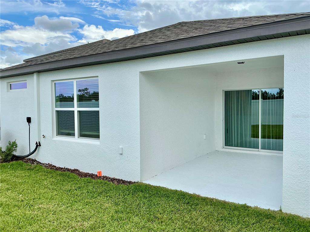 A white stucco house exterior features a covered patio, sliding glass doors, and a window — 3545 HORNBEAM ROAD, SPRING HILL, FL
