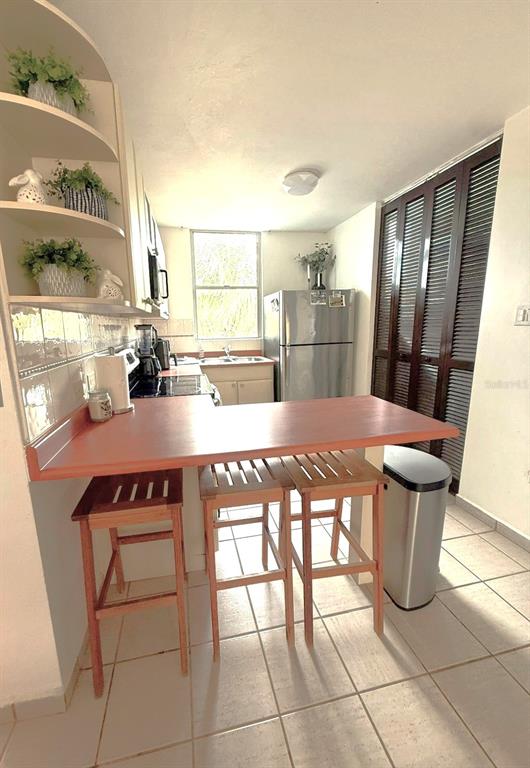 A kitchen features a breakfast bar with three wooden stools, tile flooring, and stainless appliances — COLONIA SANTA MARIA COSTA BRAVA CONDOMINIUM UNIT 8-401, CEIBA, PR