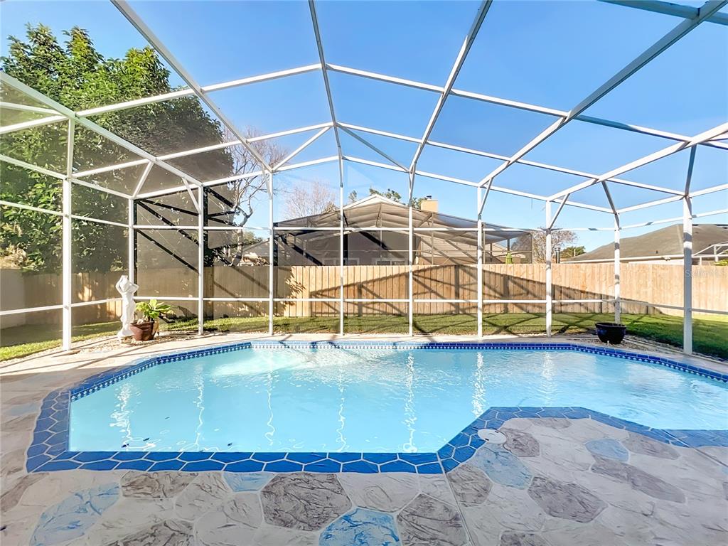 A swimming pool with a blue tiled border sits inside a screened-in patio enclosure — 9244 BEAVER COVE, APOPKA, FL