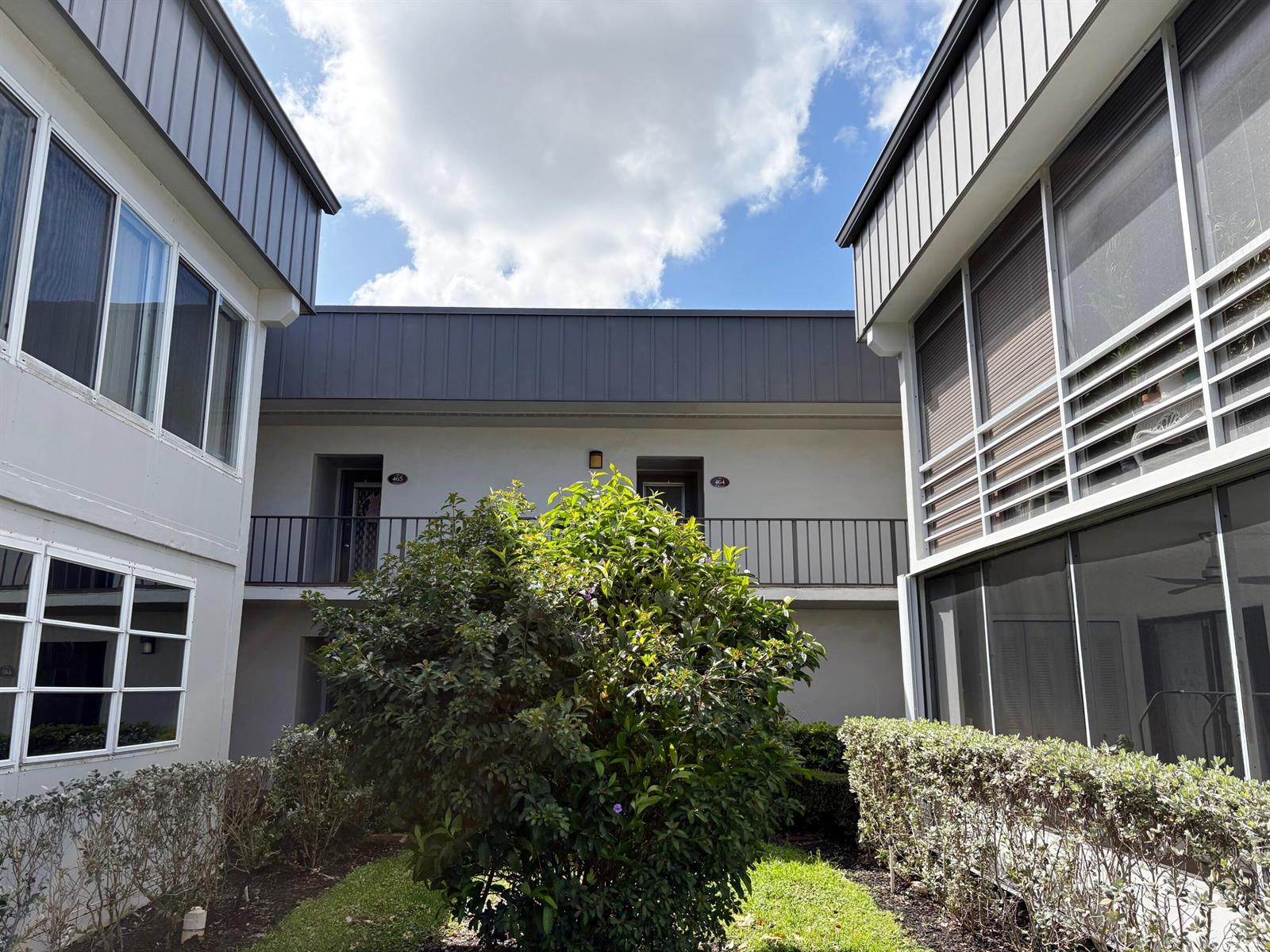 A courtyard view of a two-story apartment building with a central bush and walkways — 464 Piedmont J, Delray Beach FL 33484, DELRAY BEACH, FL