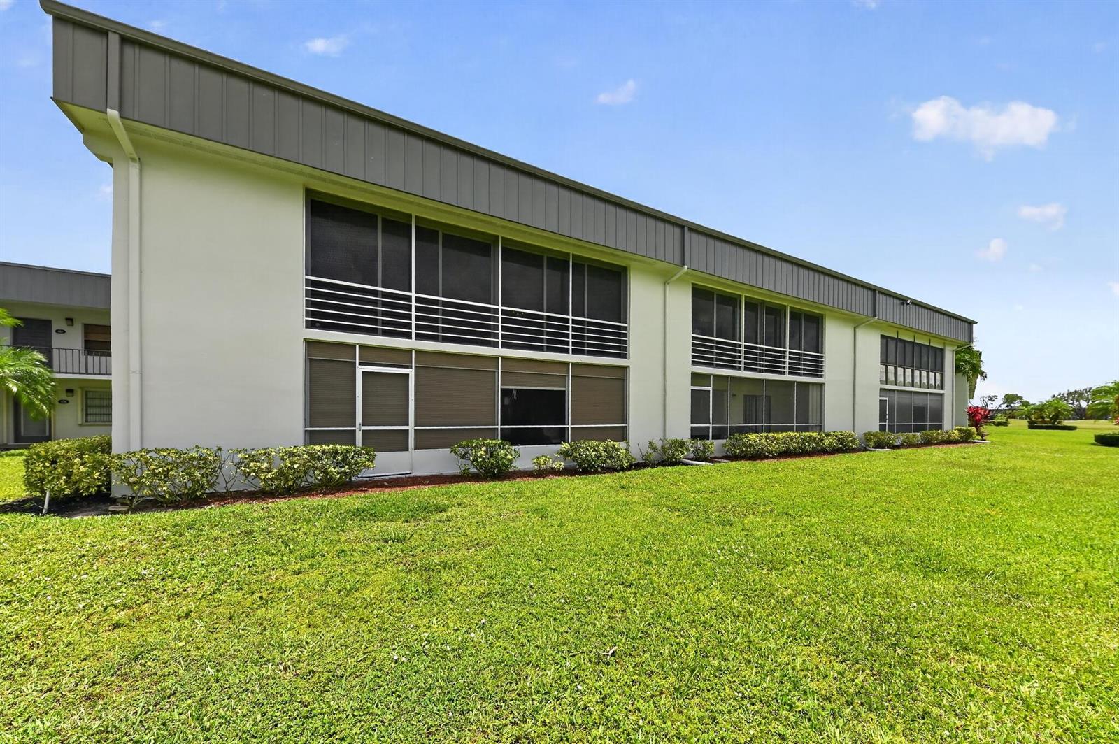 The exterior of a two-story apartment building features screened-in balconies and a grassy lawn — 464 Piedmont J, Delray Beach FL 33484, DELRAY BEACH, FL