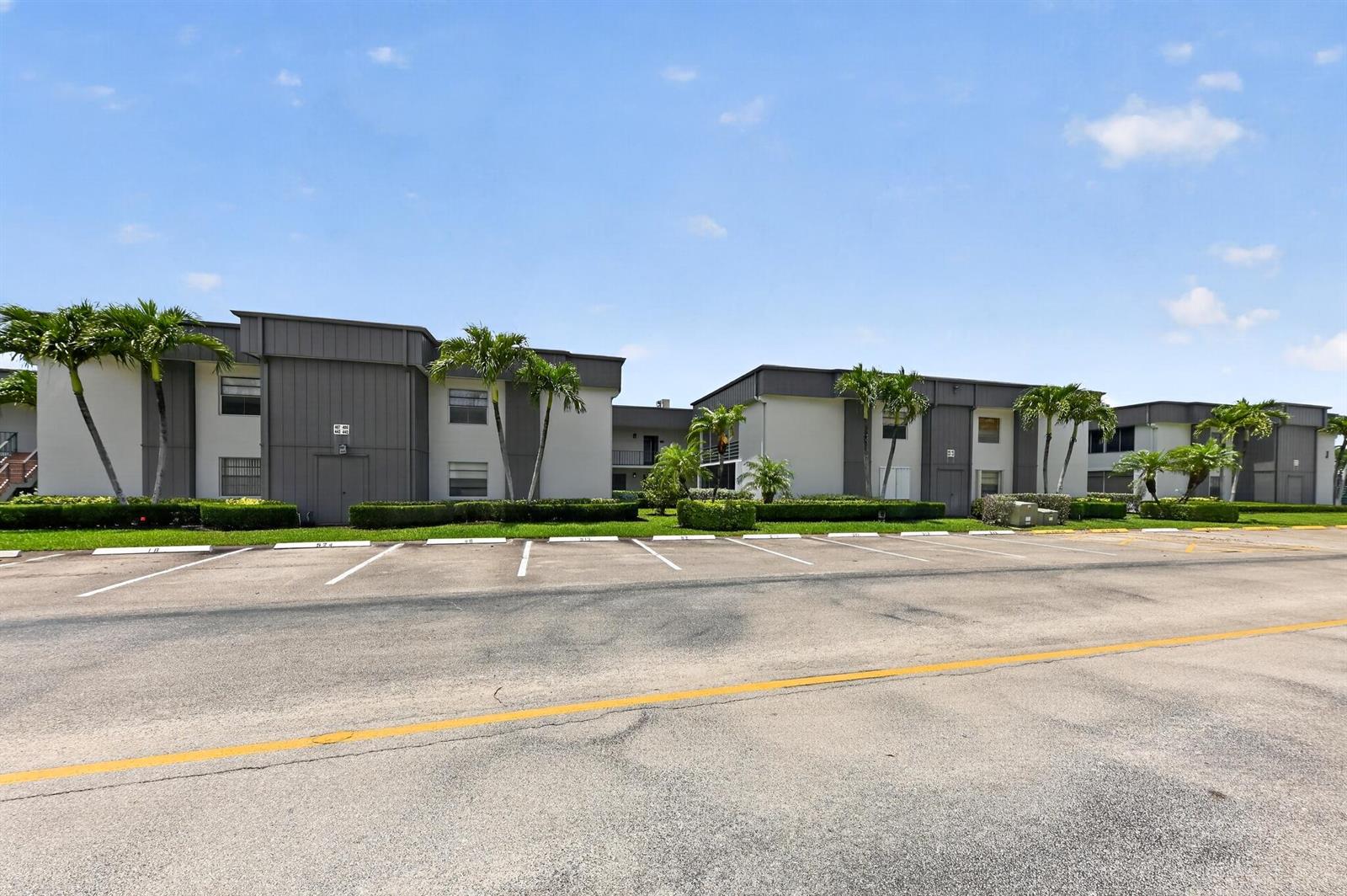 A multi-story apartment complex features gray siding, white walls, and a parking lot in front — 464 Piedmont J, Delray Beach FL 33484, DELRAY BEACH, FL