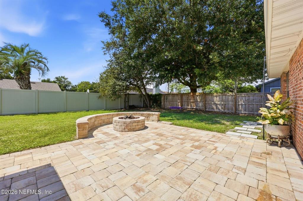 A paved patio features a stone fire pit and curved seating wall in a backyard — 12432 MUSCOVY DRIVE, JACKSONVILLE, FL