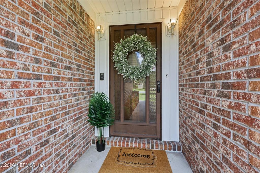 A brick-walled front entryway features a wooden door with a wreath and a welcome mat — 12432 MUSCOVY DRIVE, JACKSONVILLE, FL