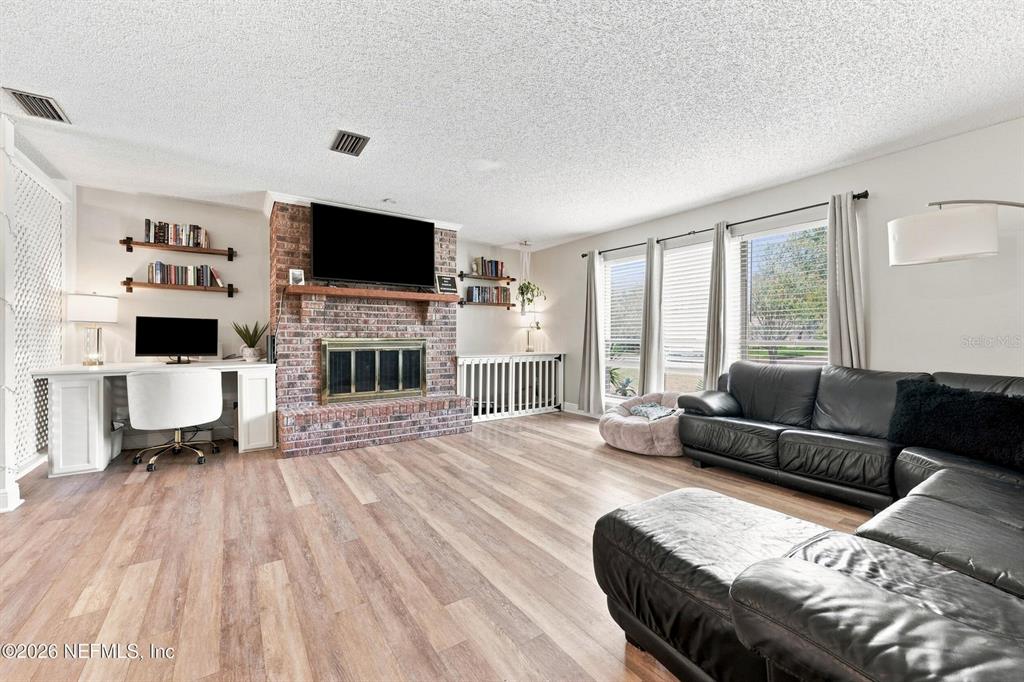 A living room features a brick fireplace, built-in desk, wood-look flooring, and a black sectional sofa — 12432 MUSCOVY DRIVE, JACKSONVILLE, FL