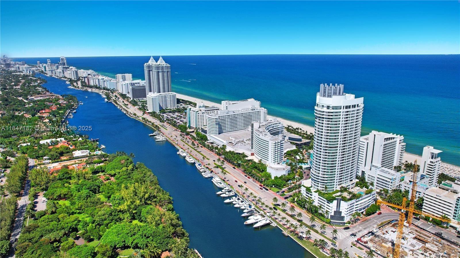 An aerial view shows a coastal city with high-rise buildings, a waterway with docked boats, and the ocean — 4401 Collins Ave, Miami Beach FL 33140, MIAMI BEACH, FL