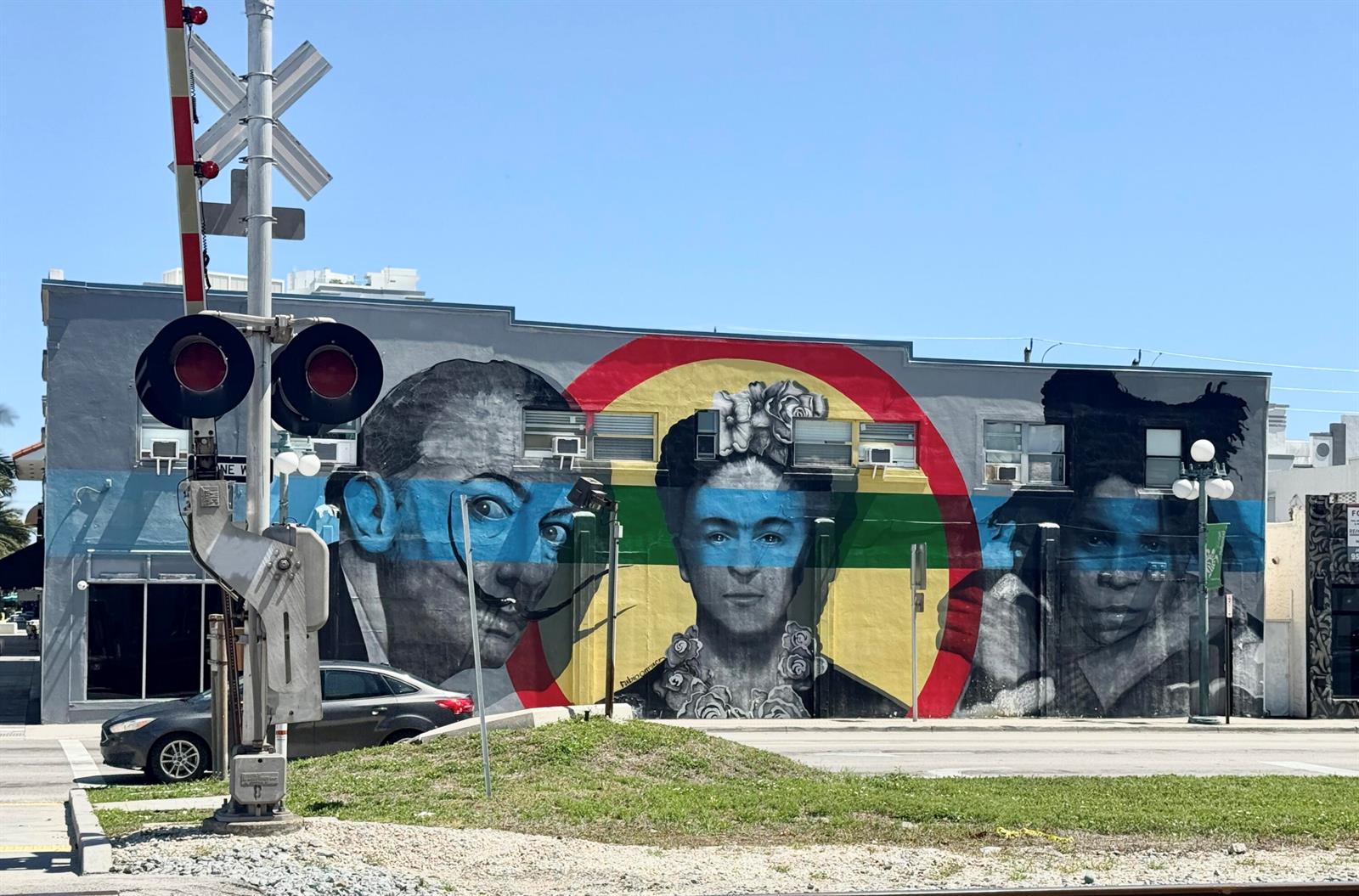 A mural of three faces painted on the exterior wall of a building near railroad tracks — 140 S Dixie Highway # 512, Hollywood FL 33020, HOLLYWOOD, FL