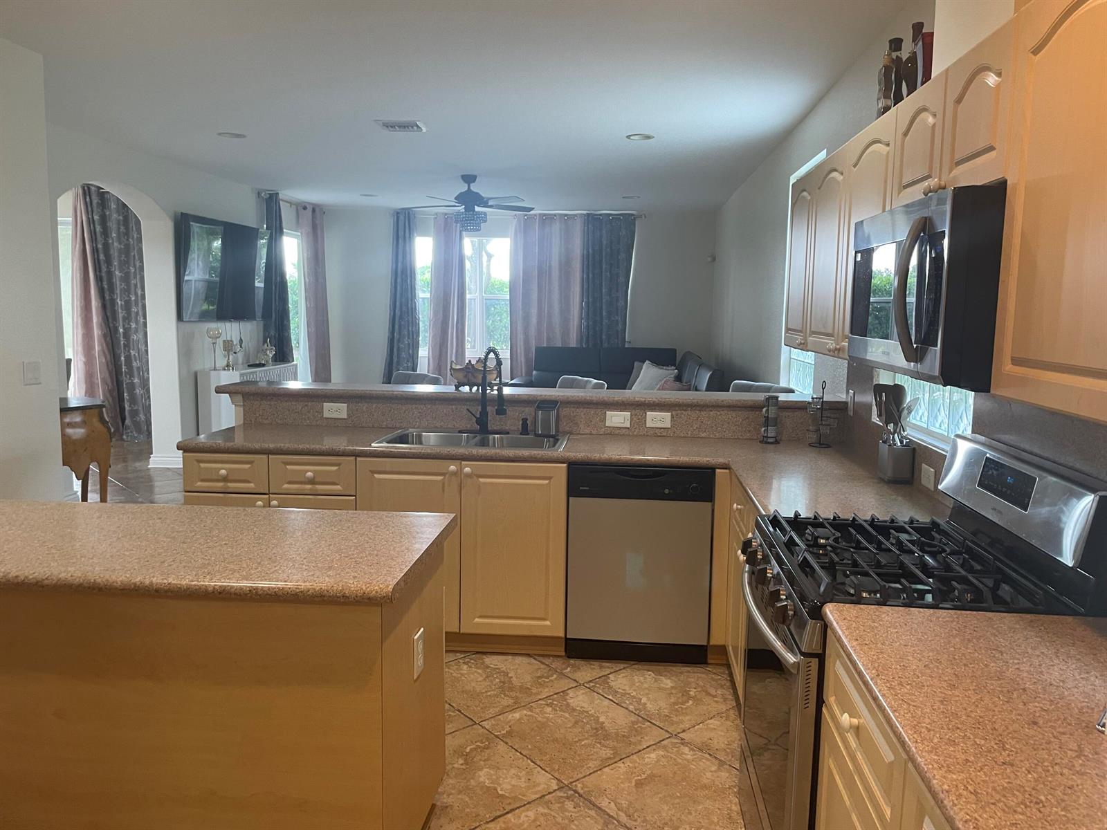 A kitchen with light wood cabinets, granite countertops, and stainless steel appliances overlooks a living area — 10690 Old Hammock Way, Wellington FL 33414, WELLINGTON, FL