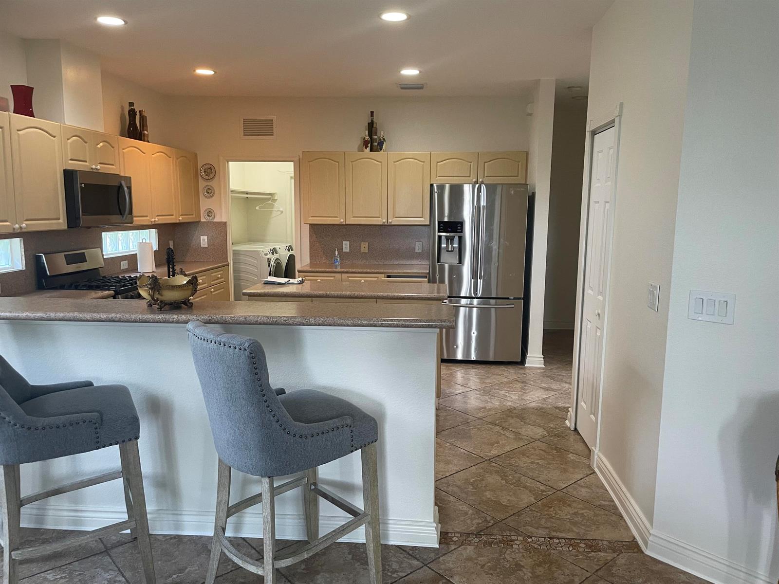 A kitchen features light wood cabinets, stainless steel appliances, a breakfast bar, and tile flooring — 10690 Old Hammock Way, Wellington FL 33414, WELLINGTON, FL