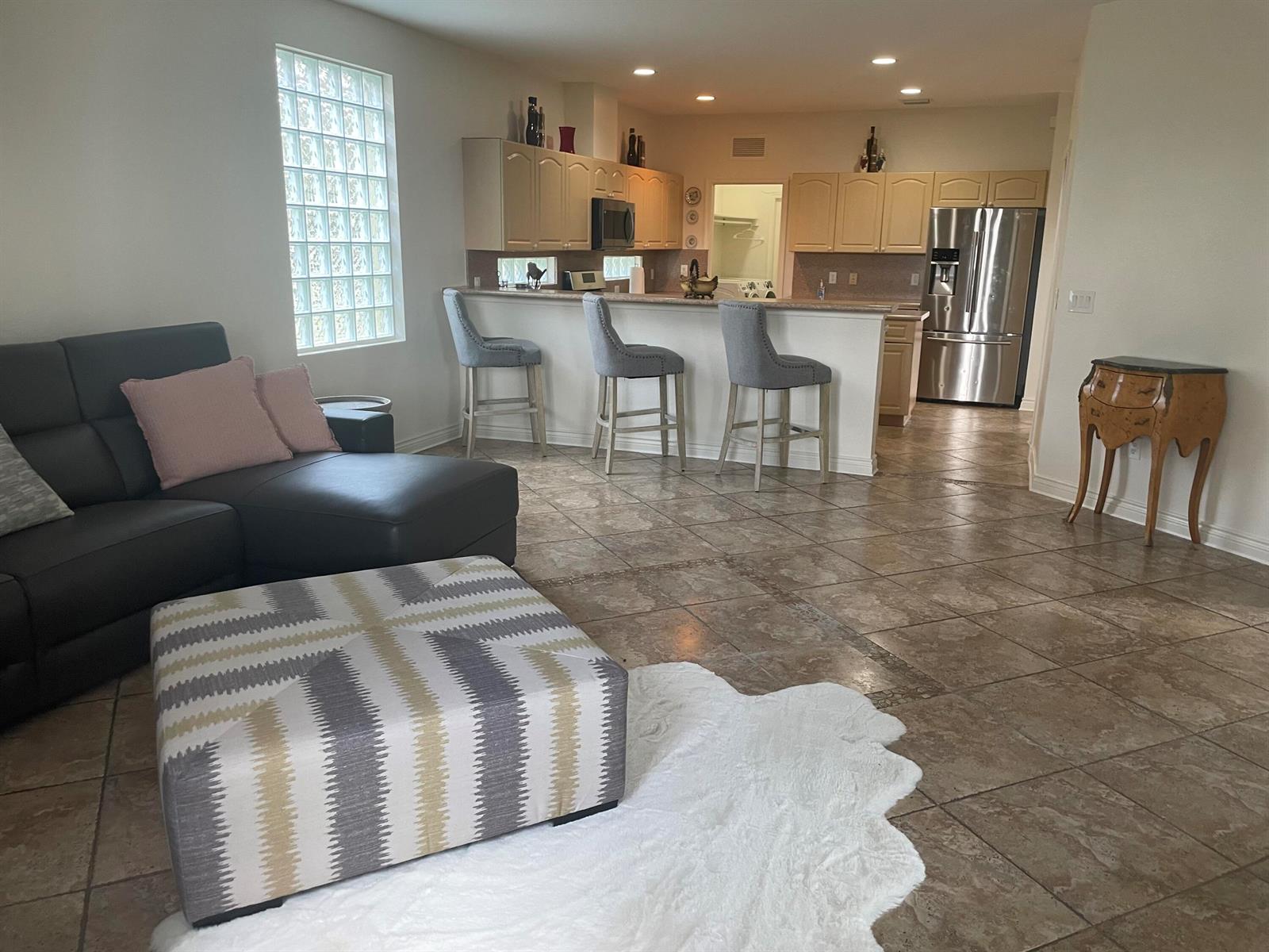 An open-concept living room and kitchen featuring tile floors, a sectional sofa, and bar seating — 10690 Old Hammock Way, Wellington FL 33414, WELLINGTON, FL