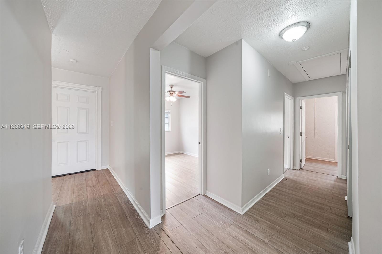A hallway with light wood-look flooring leads to several doorways and a bedroom — 1000 NW 17th Ave, Boca Raton FL 33486, BOCA RATON, FL