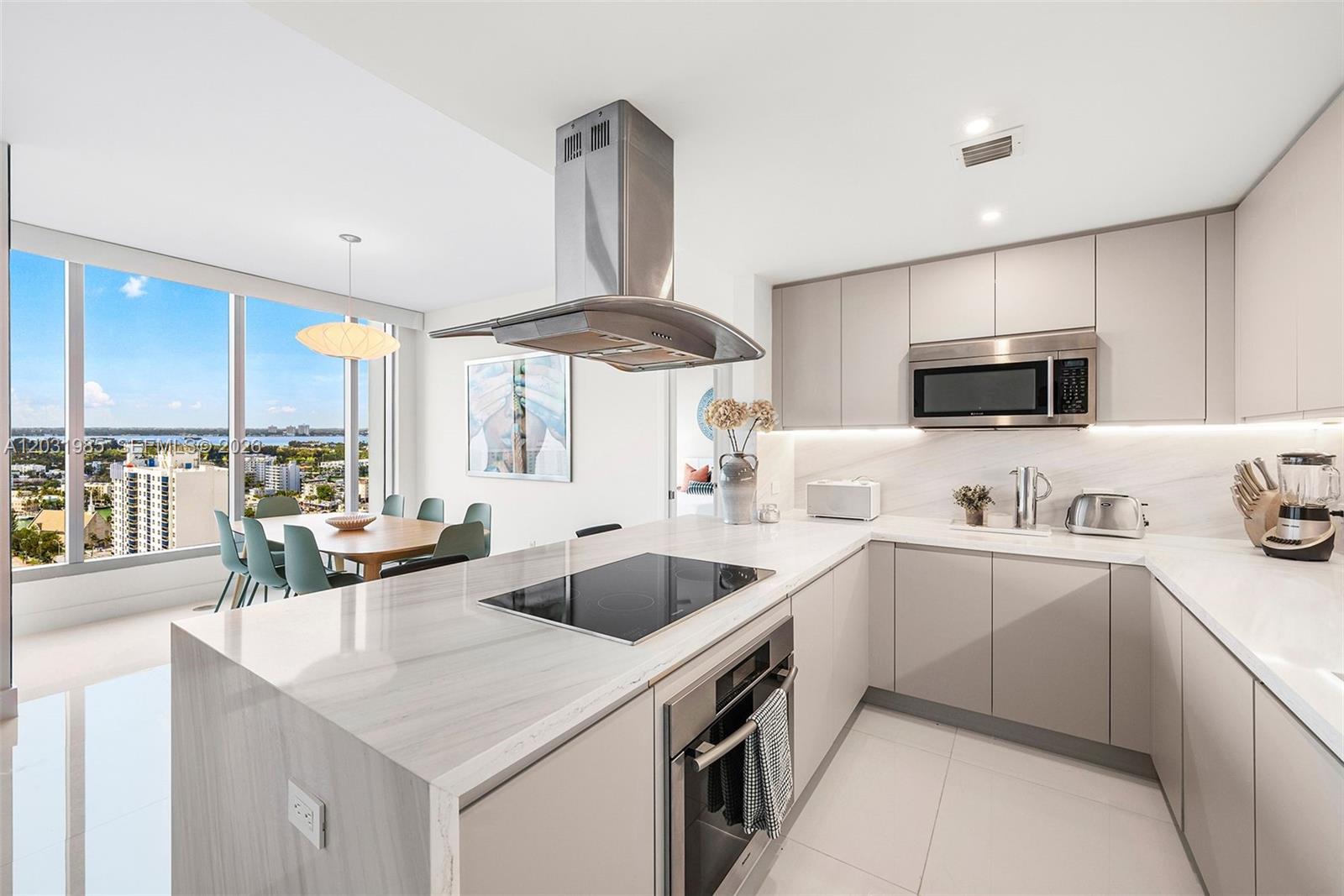 A modern kitchen features light-toned cabinetry, marble countertops, stainless steel appliances, and a dining area — 6899 Collins Ave # 1903, Miami Beach FL 33141, MIAMI BEACH, FL