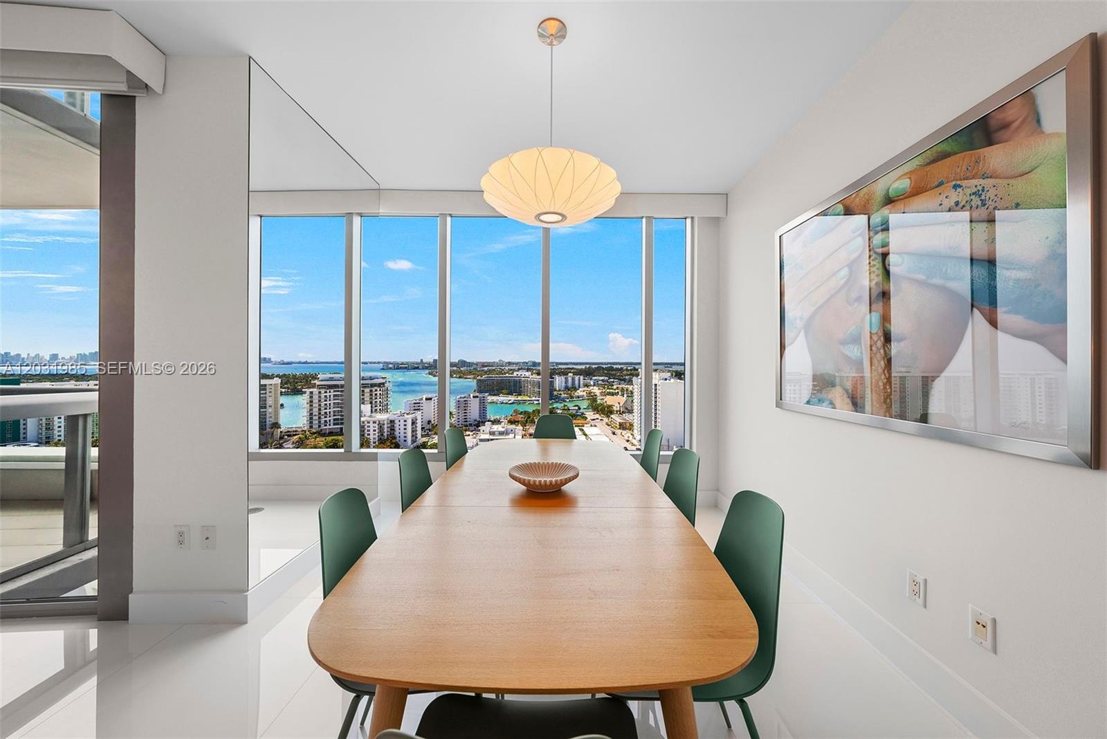 A dining room features a wooden table, green chairs, and floor-to-ceiling windows overlooking the water — 6899 Collins Ave # 1903, Miami Beach FL 33141, MIAMI BEACH, FL
