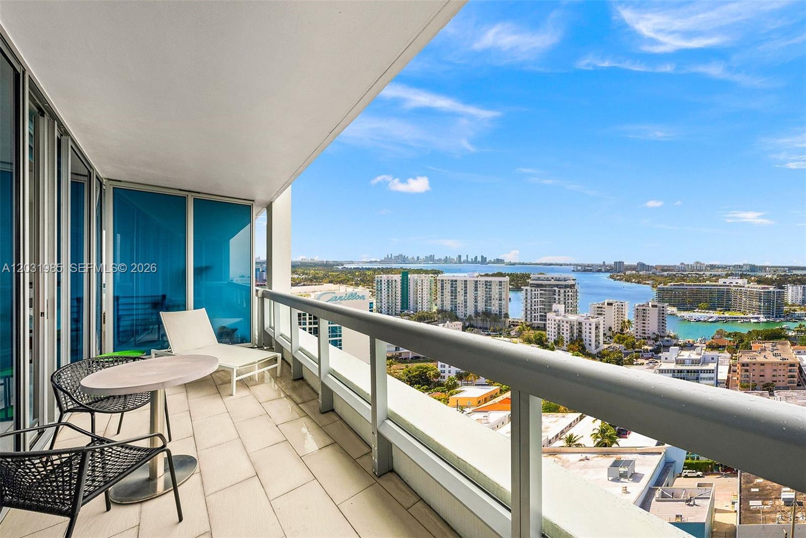A balcony with outdoor furniture overlooks a coastal city skyline and a body of water — 6899 Collins Ave # 1903, Miami Beach FL 33141, MIAMI BEACH, FL