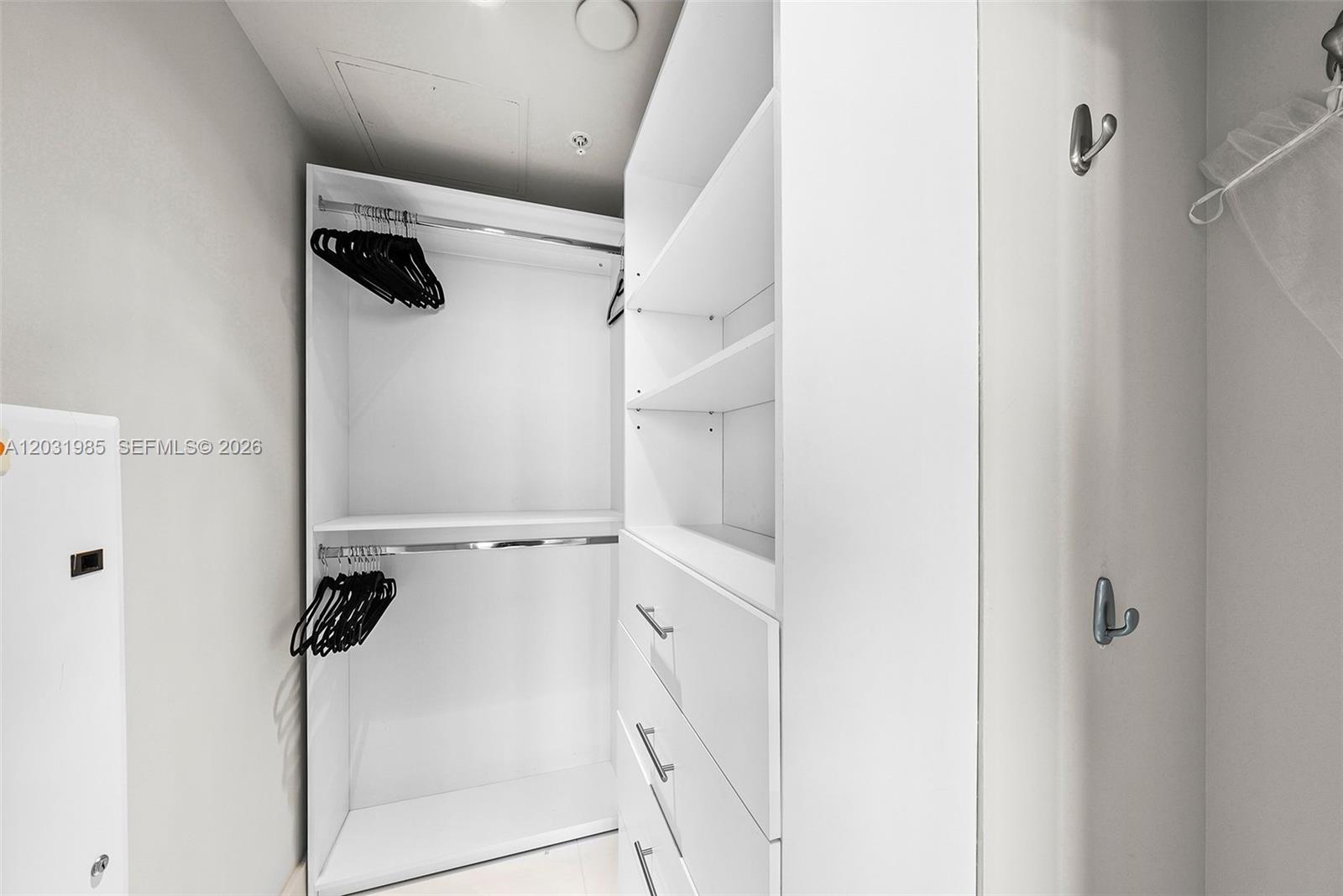 A walk-in closet features white shelving, hanging rods with black hangers, and built-in drawers — 6899 Collins Ave # 1903, Miami Beach FL 33141, MIAMI BEACH, FL