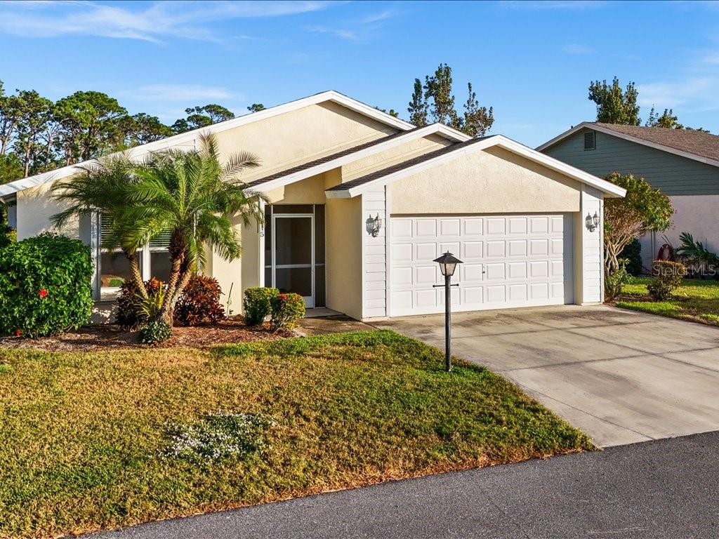 A single-story house with a beige stucco exterior, a two-car garage, and a palm tree — 515 WEKIVA RIVER COURT UNIT 81, ENGLEWOOD, FL