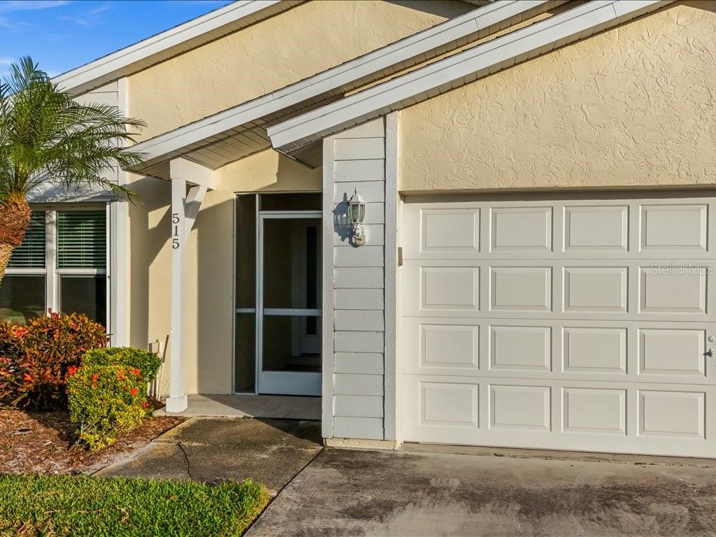 A beige house exterior features a white garage door, a screened entryway, and landscaping — 515 WEKIVA RIVER COURT UNIT 81, ENGLEWOOD, FL