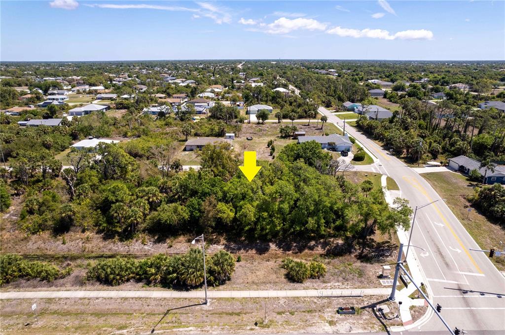 An aerial view shows a wooded, undeveloped lot marked by a yellow arrow near a road — 7679 CASTLEBERRY TERRACE, ENGLEWOOD, FL