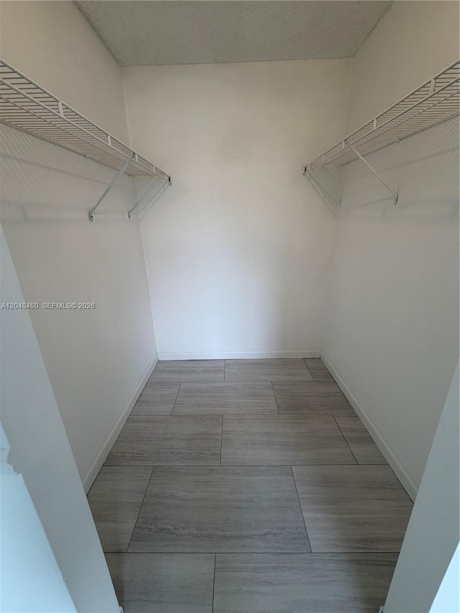 A walk-in closet features white walls, wire shelving on both sides, and light-colored tile flooring — 1175 NW 123rd Pl # 210, Miami FL 33182, MIAMI, FL