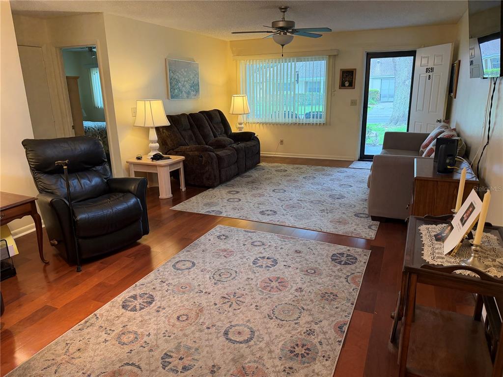 A living room features hardwood floors, two patterned area rugs, and multiple seating options — 8591 SW 93RD PLACE UNIT B, OCALA, FL