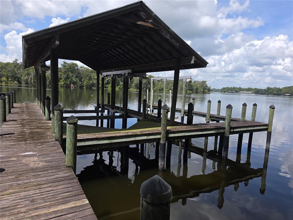 A wooden boat dock with a covered slip extends into a calm lake — 123 WHITNEY STREET, SATSUMA, FL