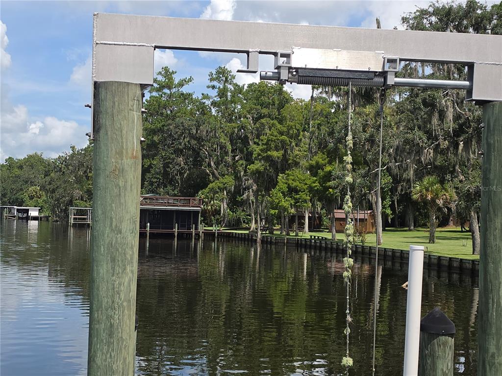 A boat lift mechanism is mounted on wooden pilings overlooking a canal and wooded shoreline — 123 WHITNEY STREET, SATSUMA, FL