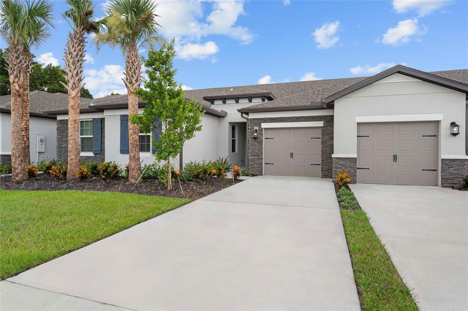 A single-story house exterior features a two-car garage, stone accents, and three palm trees — 1609 Celebration Drive, Fort Pierce FL 34947, FORT PIERCE, FL