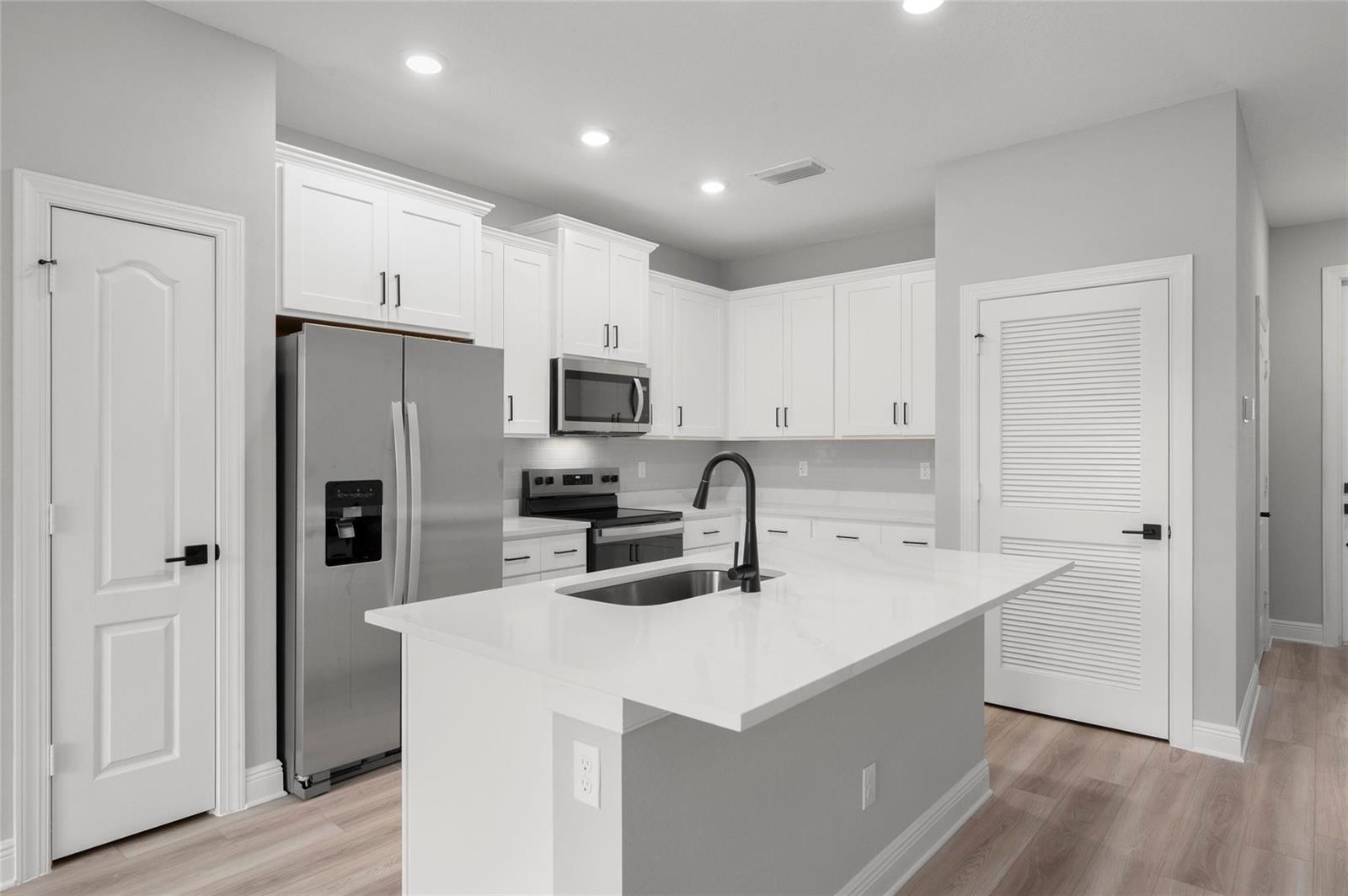 A modern kitchen features white cabinetry, stainless steel appliances, a center island, and light flooring — 1609 Celebration Drive, Fort Pierce FL 34947, FORT PIERCE, FL