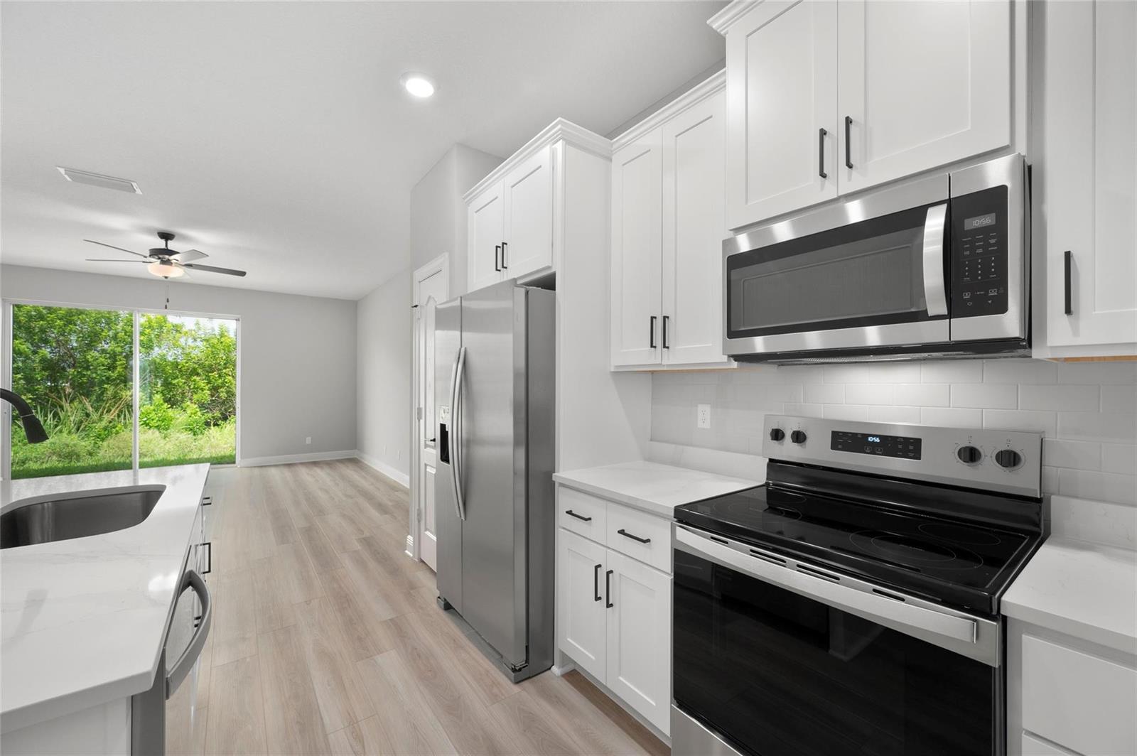 A modern kitchen features white cabinets, stainless steel appliances, and light wood-look flooring — 1609 Celebration Drive, Fort Pierce FL 34947, FORT PIERCE, FL