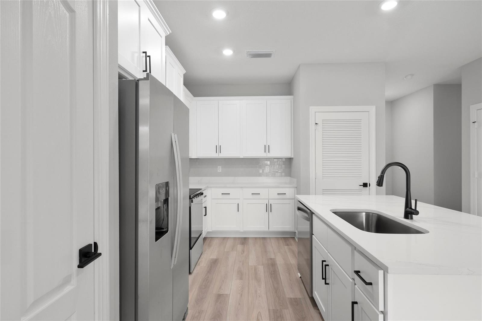 A modern kitchen features white cabinetry, stainless steel appliances, and a central island with sink — 1609 Celebration Drive, Fort Pierce FL 34947, FORT PIERCE, FL