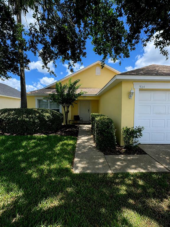 A yellow house with a white garage door and a concrete walkway leading to the entrance — 324 CASTERTON CIRCLE, DAVENPORT, FL